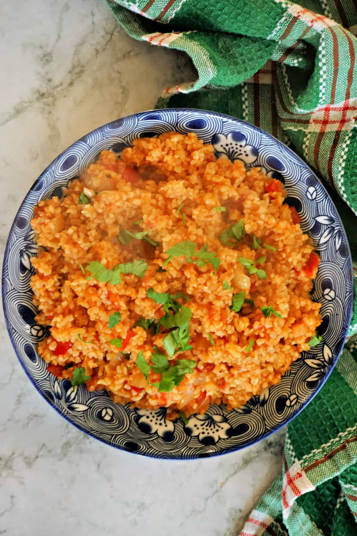 A blue plate with ulgur pilaf and a green tea towel around the plate.