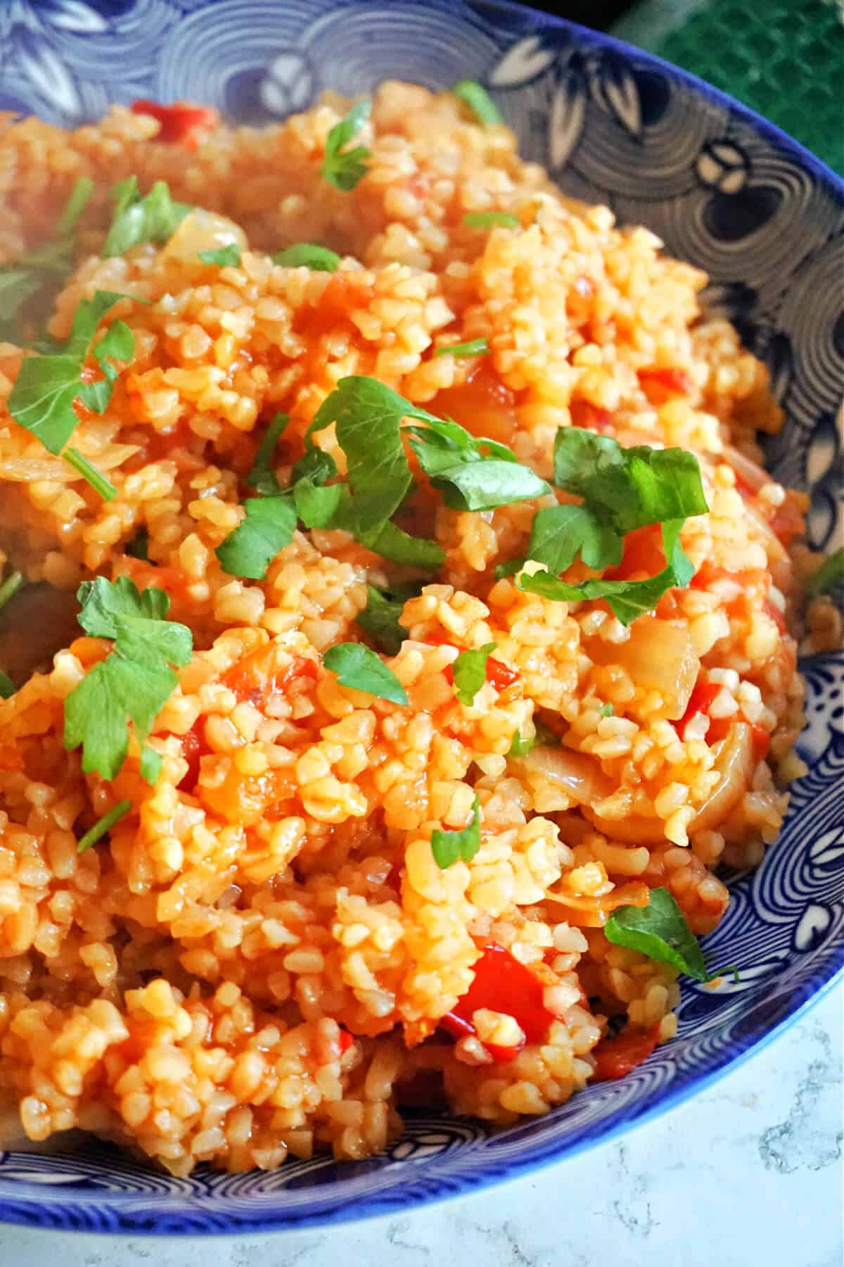 A blue plate with bulgur pilaf garnished with chopped parsley.