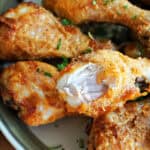 A plate with golden chicken drumsticks with one drumstick having a bite off it.