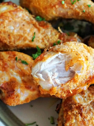 A plate with golden chicken drumsticks with one drumstick having a bite off it.