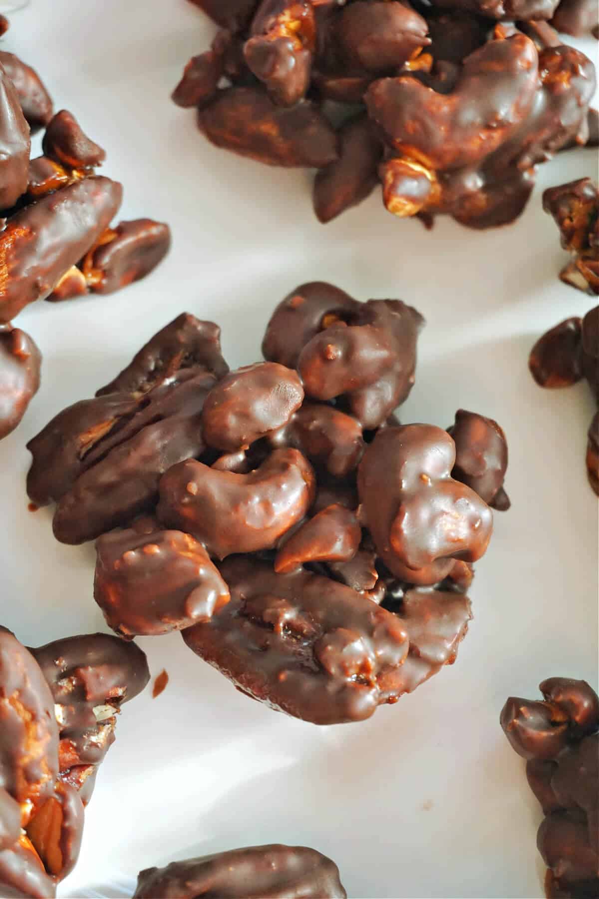 A white plate with a chocolate nut cluster with other clusters partially visble.