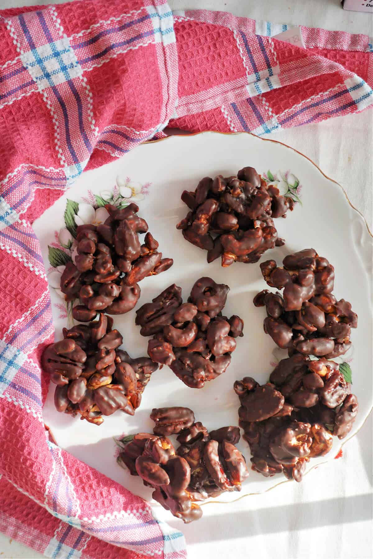 A white plate with 7 chocolate nut clusters and a pink tea towel around it.