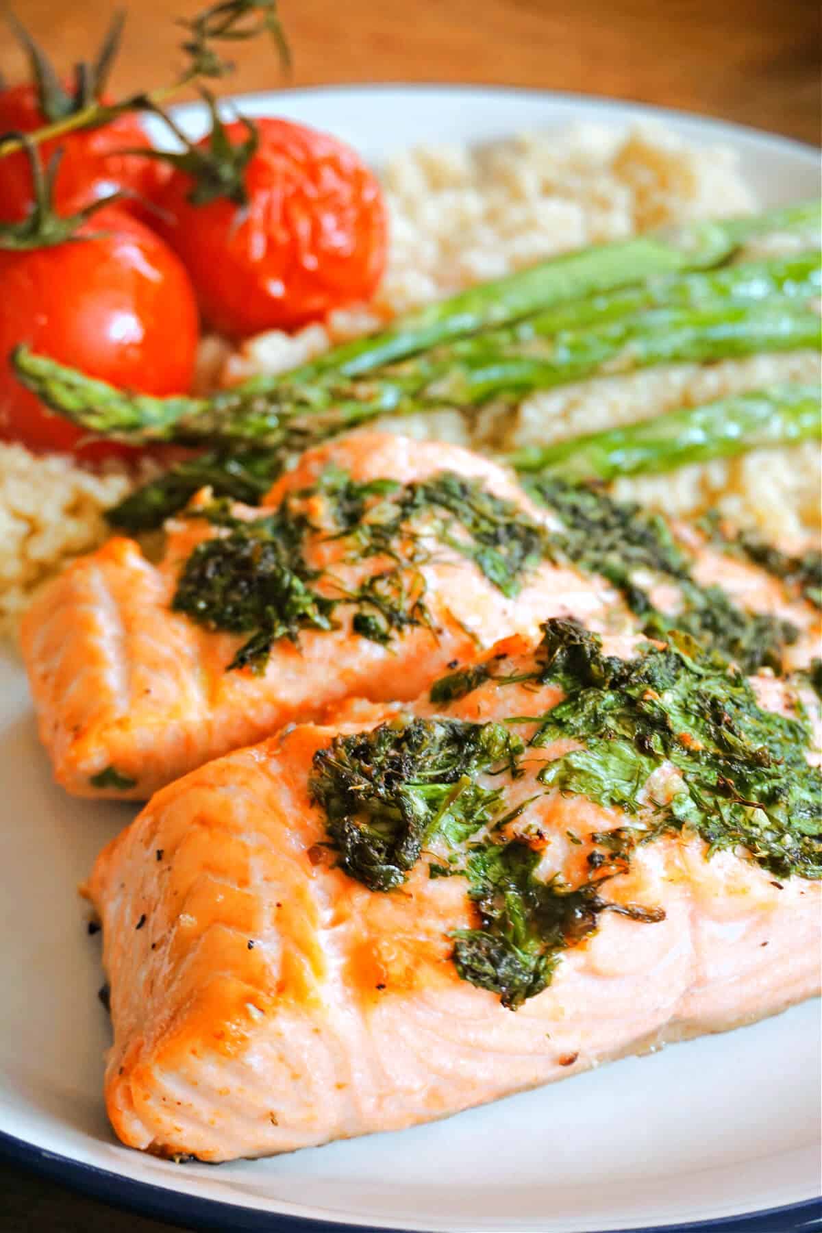 A plate with 2 salmon fillets topped with herbs, asparagus and 2 roasted tomatoes.