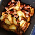 An air fryer drawer with cooked potatoe wedges and sausage cut into chunks.