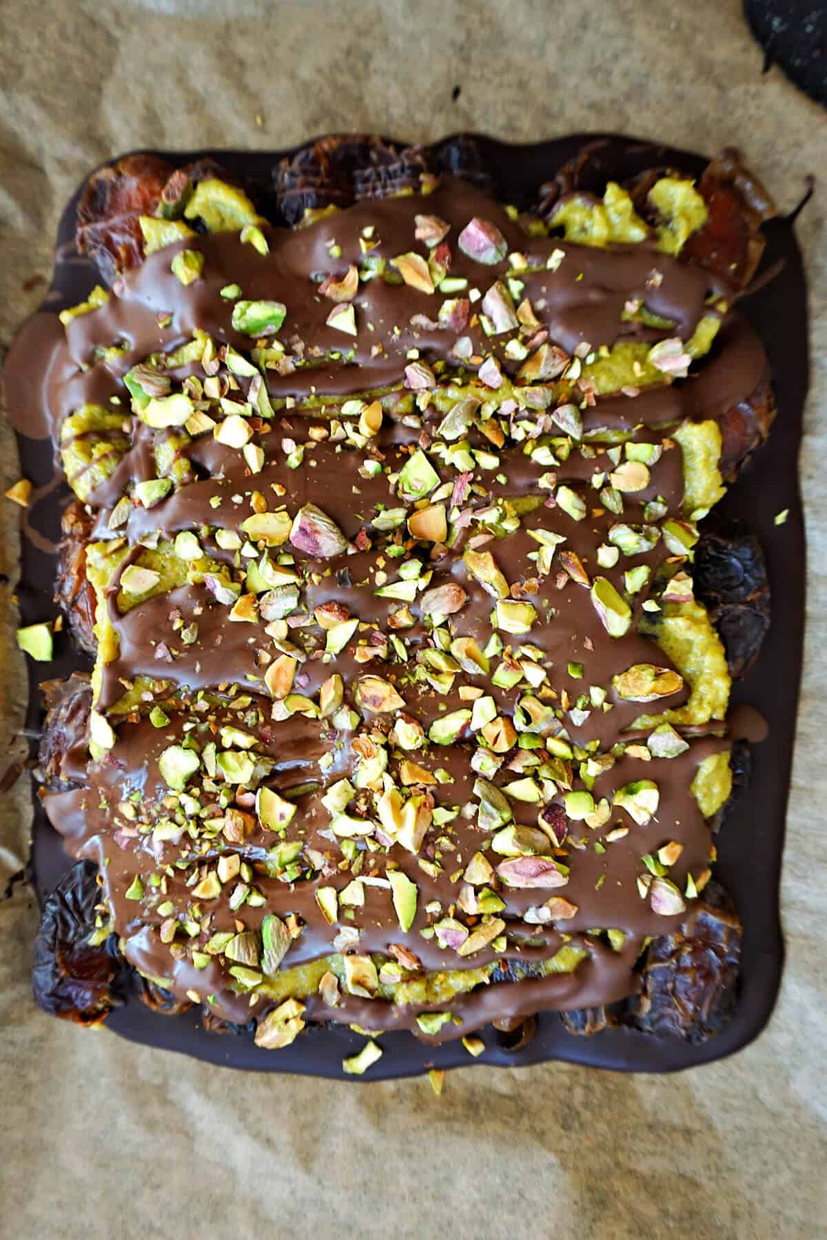 A baking tray with a chocolate bark topped with chopped pistachios.
