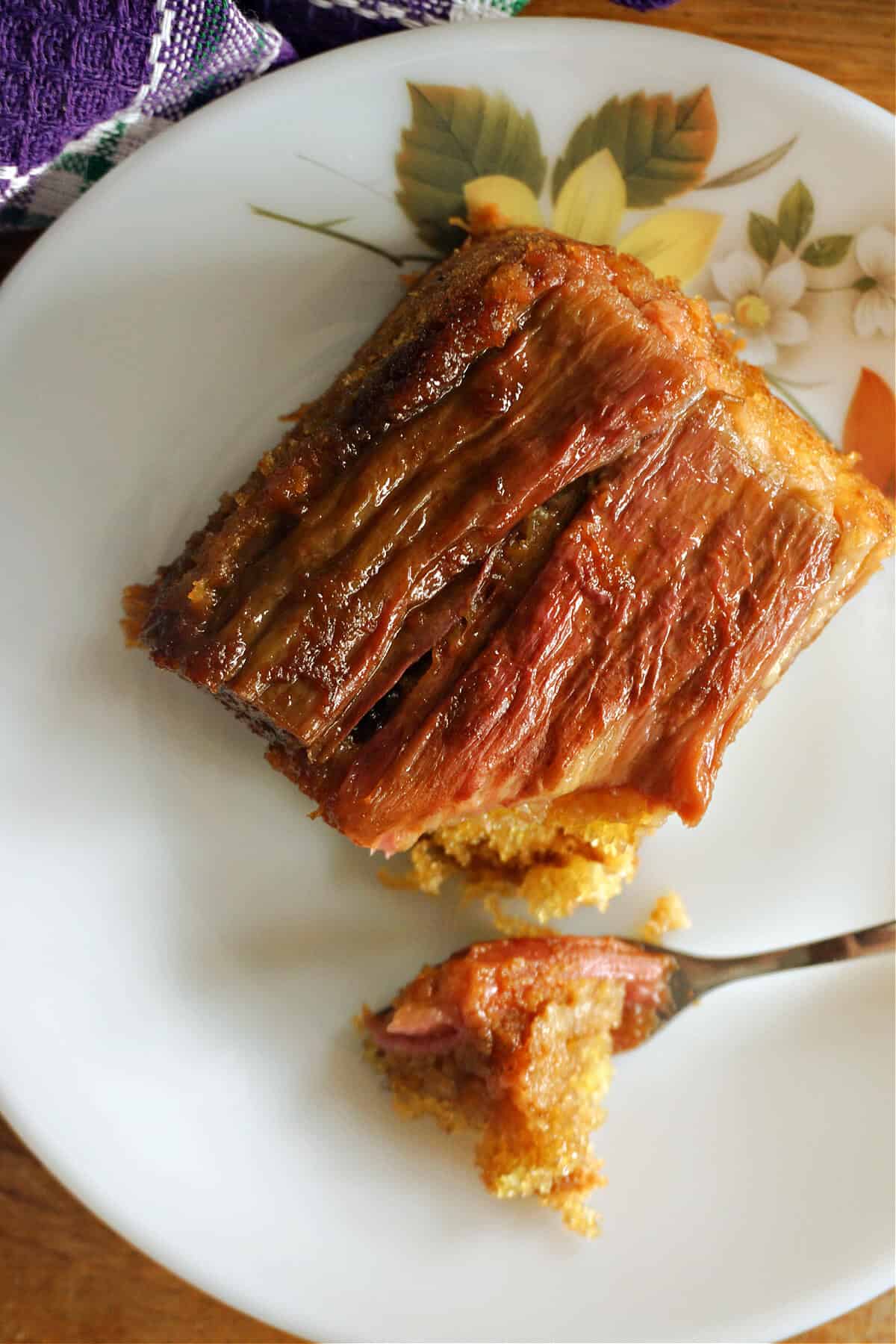 A slice of rhubarb cake and a fork with a bite of the cake on a white plate.