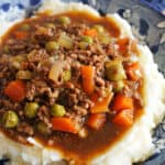 A blue patterned plate with mince and gravy with veggies over a bed of mash.