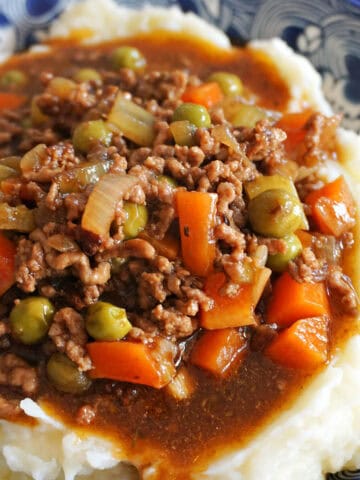 A blue patterned plate with mince and gravy with veggies over a bed of mash.