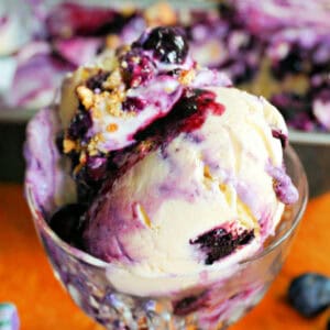A glass cup with scoops of blueberry ice cream topped with crushed biscuits.