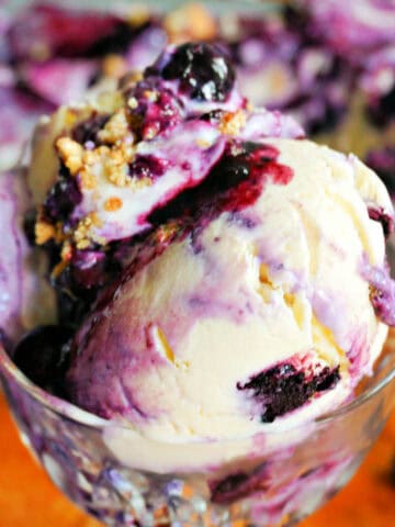 A glass cup with scoops of blueberry ice cream topped with crushed biscuits.