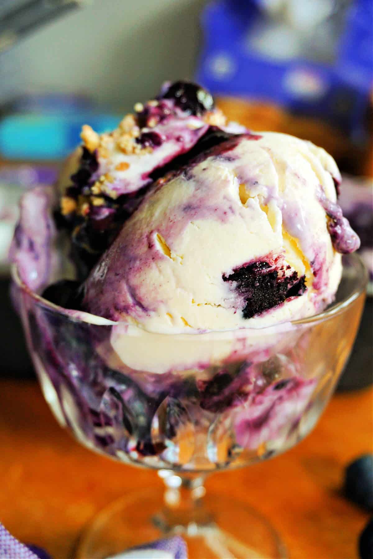 A glass cup with blueberry ice cream topped with crushed biscuits.