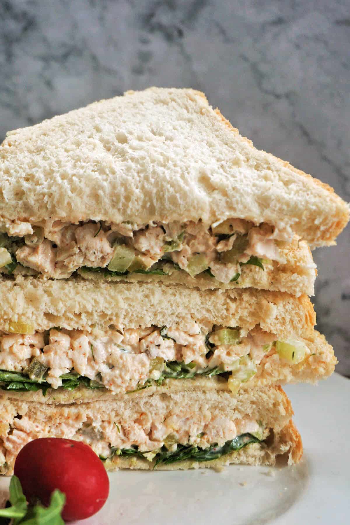 A stack of chicken sandwich triangles on a white plate.