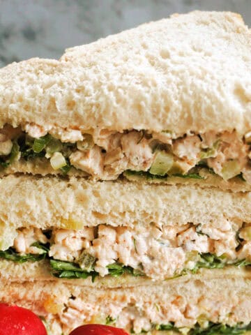 A stack of chicken sandwiches cut into triangles with 2 radishes in front of them.