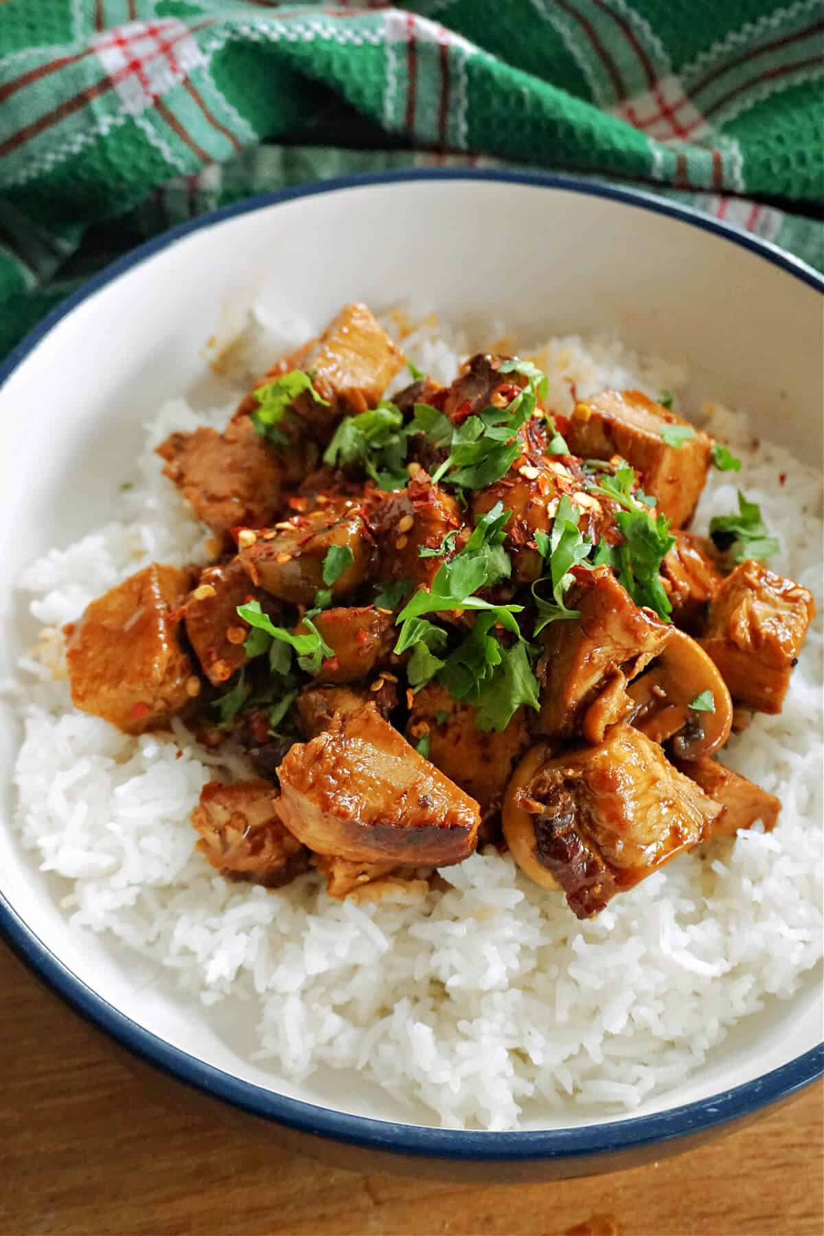 A white bowl with pork stir fry harnished with parsley on top of a bed of rice