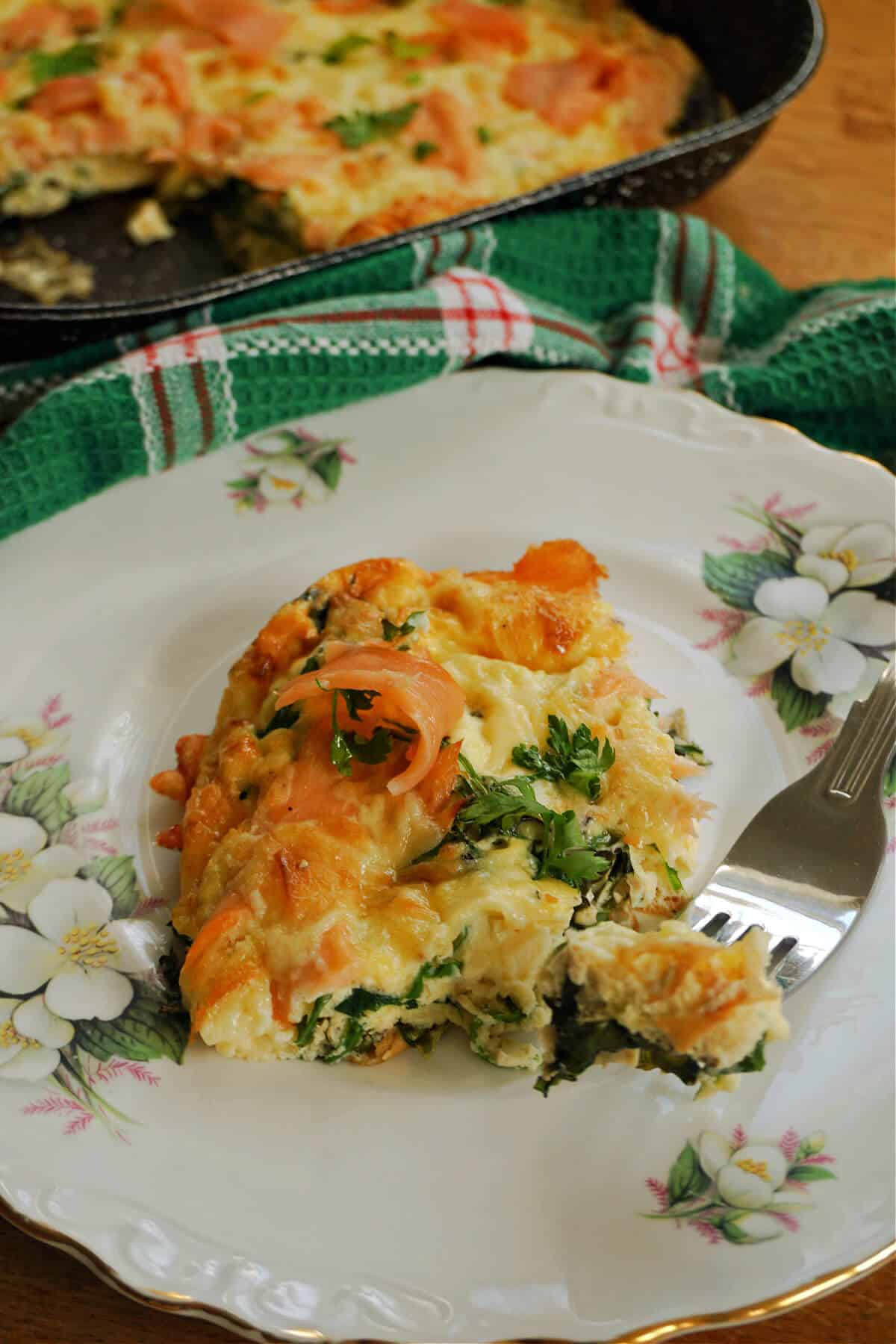 A slice of frittata on a flowery plate with a green tea towel around.