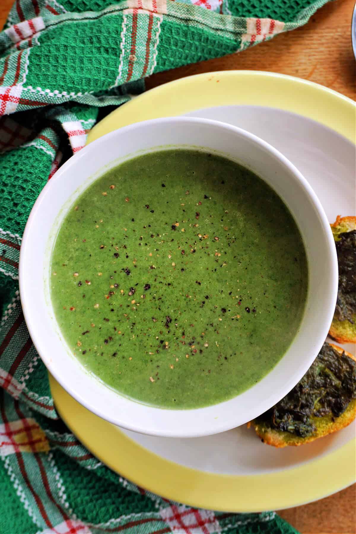 A white bowl with cream of nettle soup garnished with ground black pepper.