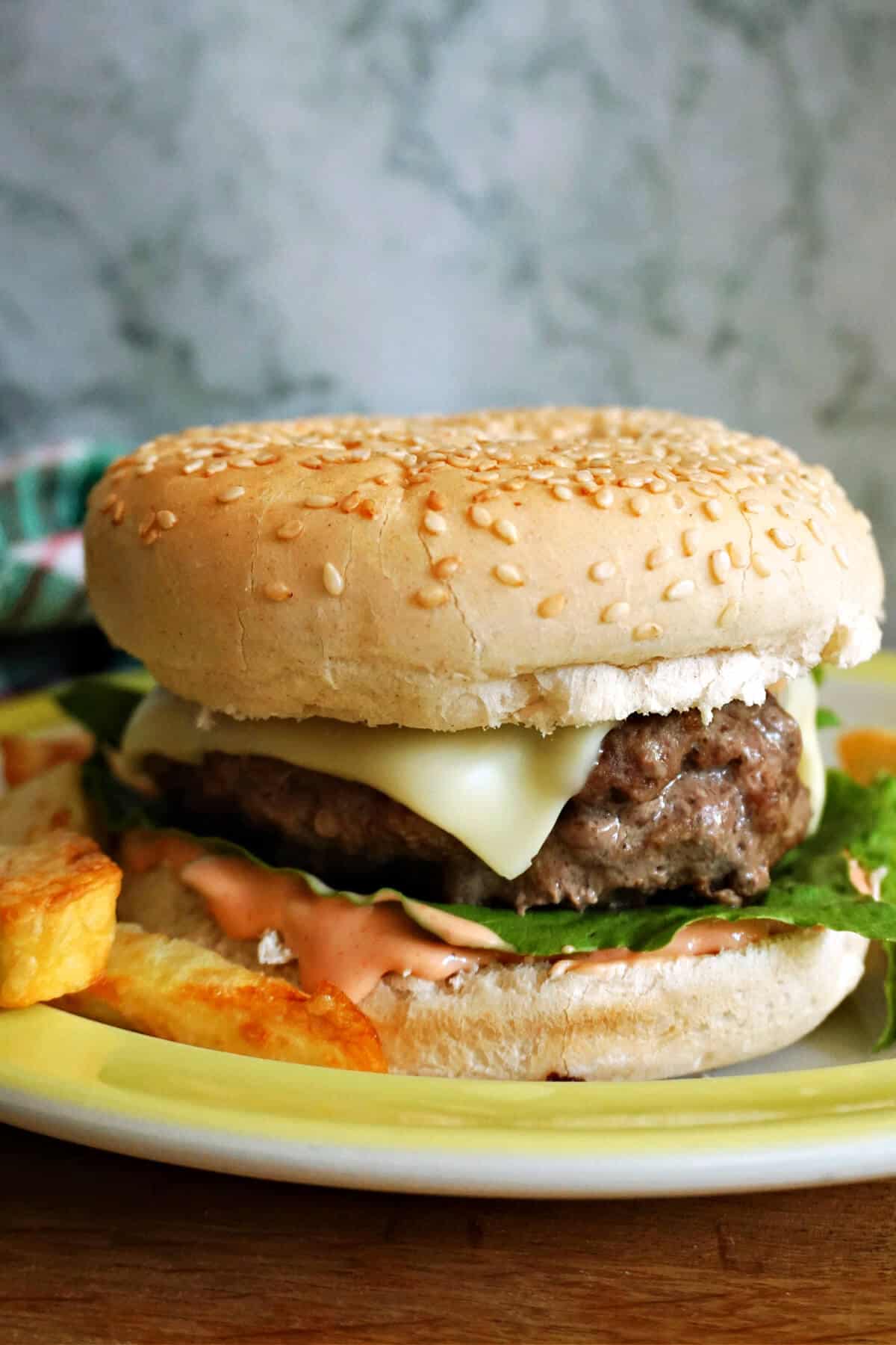 A cheeseburger on a plate with partially-visible fries around it.