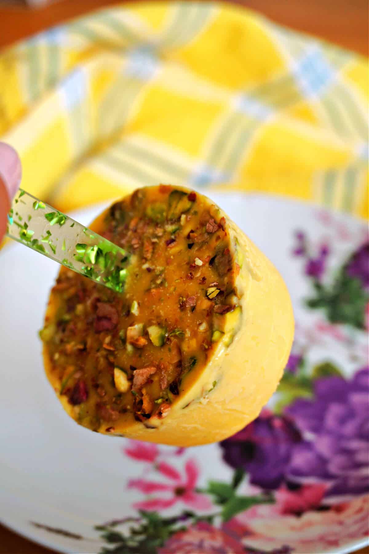 A hand holding a mango popsicle over a white flowery plate. A yellow-pattered tea towel is around the plate.