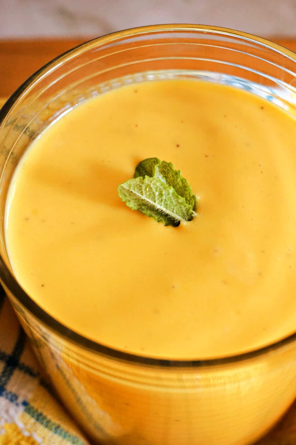 A glass with mango lassi garnished with mint leaves.