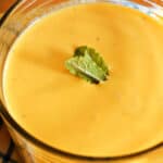 A glass of mango lassi garnished with mint leaves.