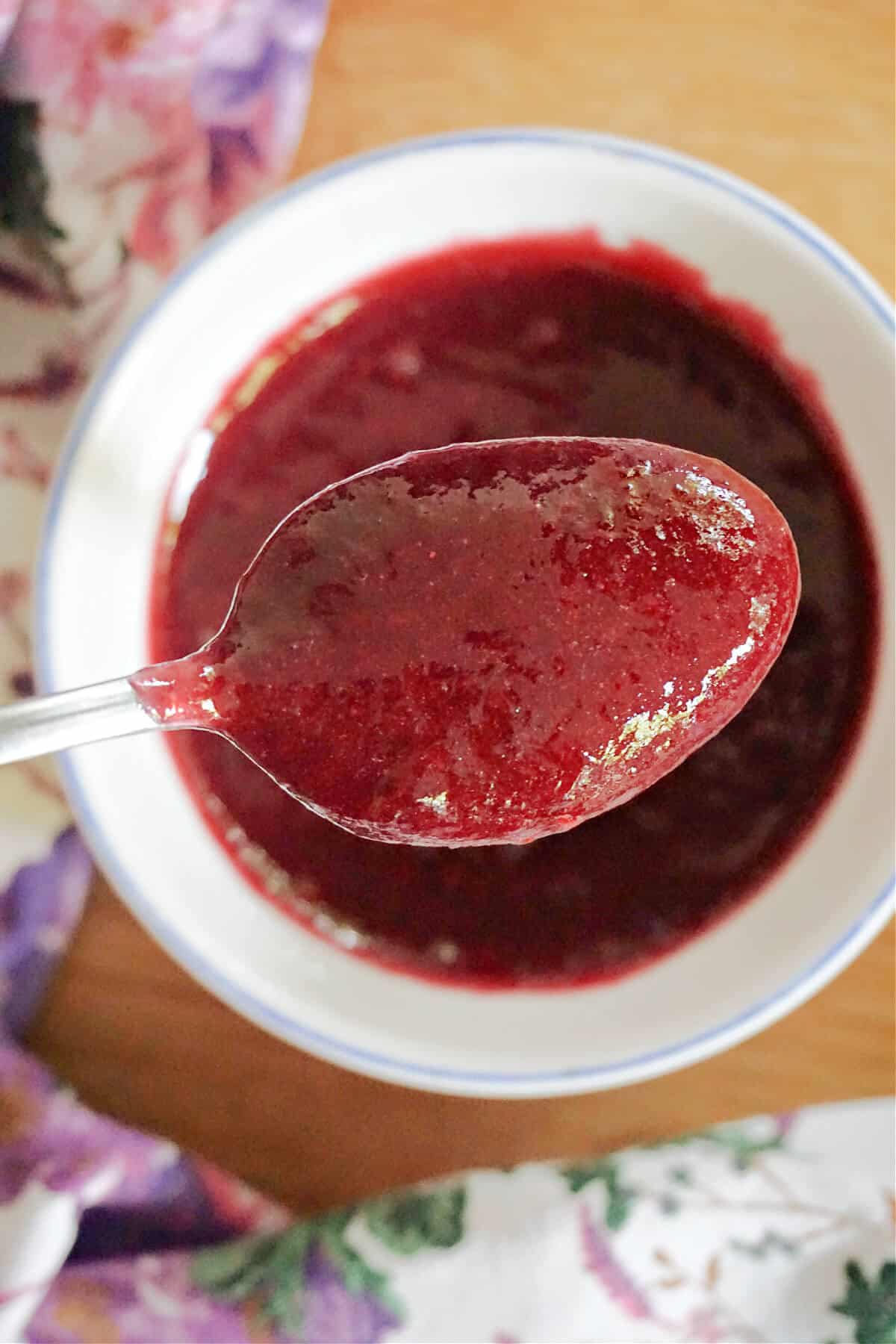 A spoonful of jam with a ramekin of jam in the background.