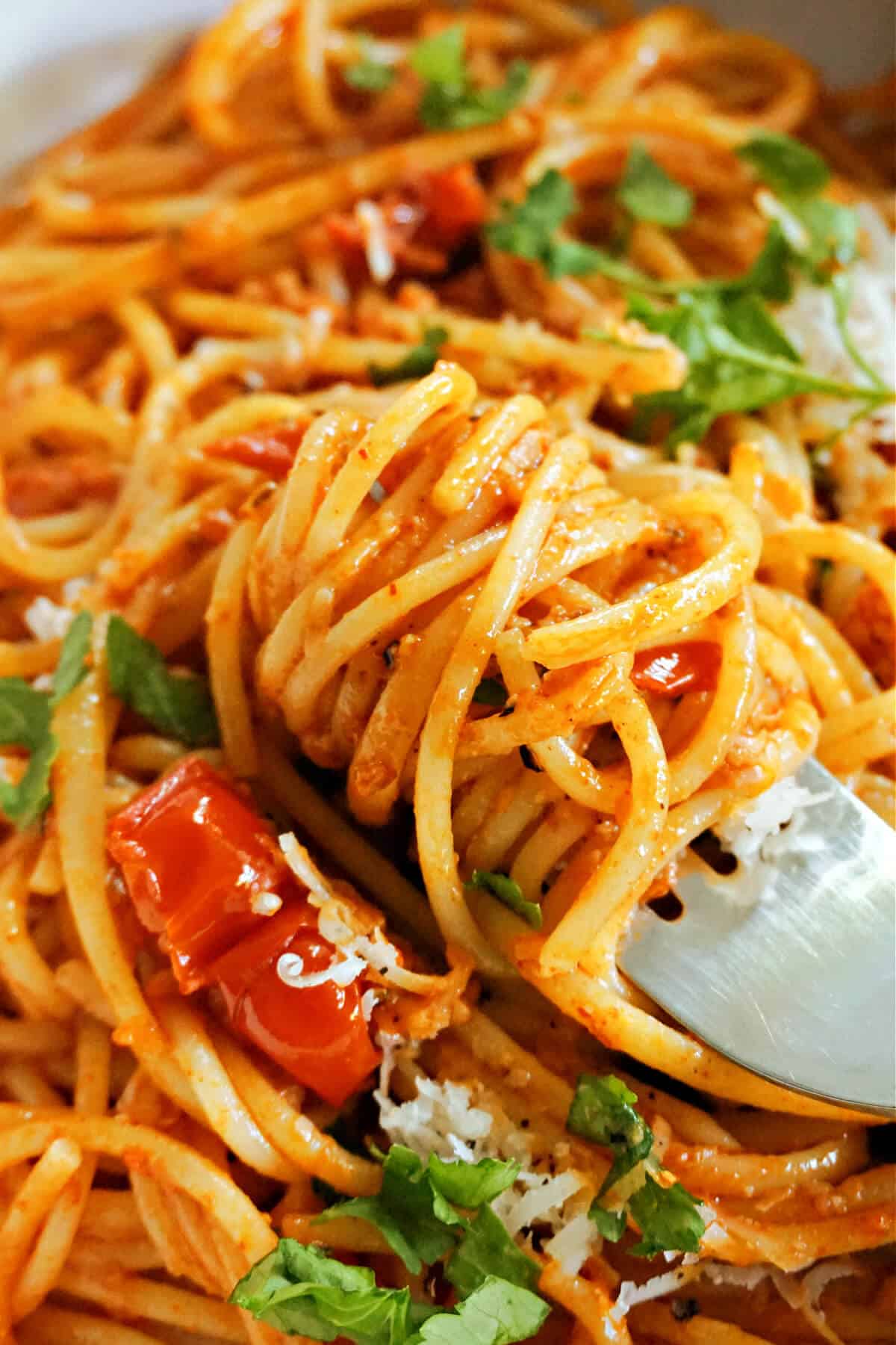 Close-up of a fork twisting spaghetti cooked in a red sauce.