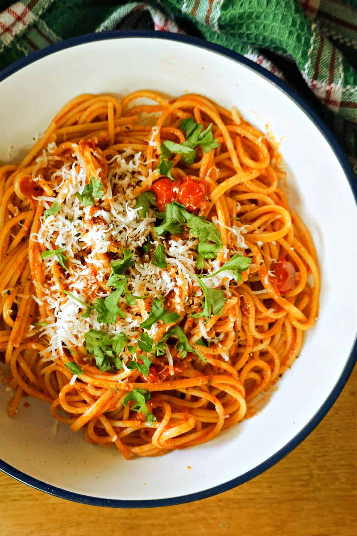 A white bowl with pasta in sauce garnished with parmesan and chopped parsley.