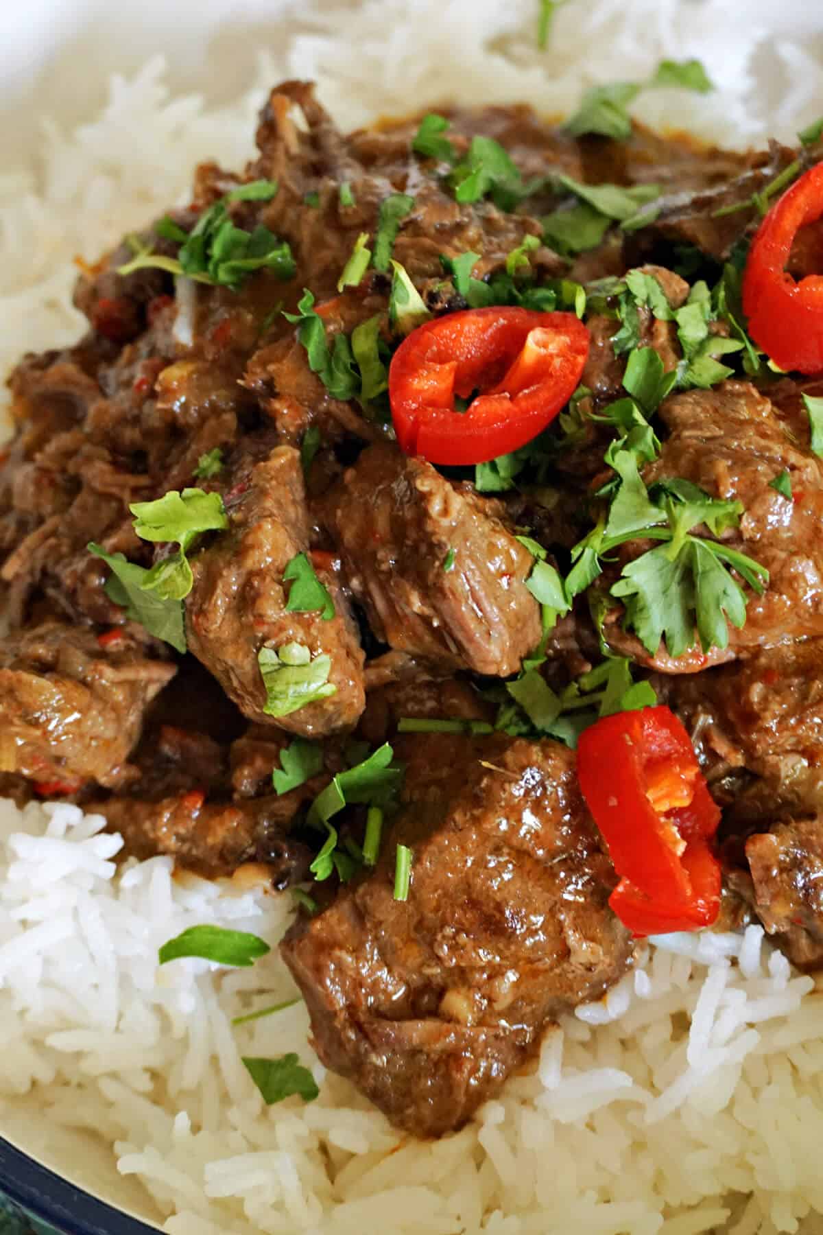 A beef curry topped with chopped coriander and 3 slices of red chillies on a bed or rice.