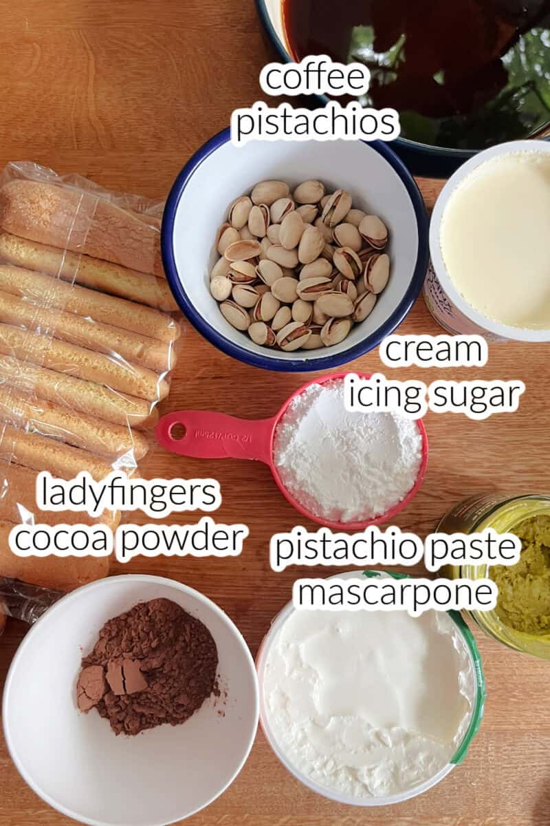 A wooden table with ingredients needed to make pistachio tiramisu.