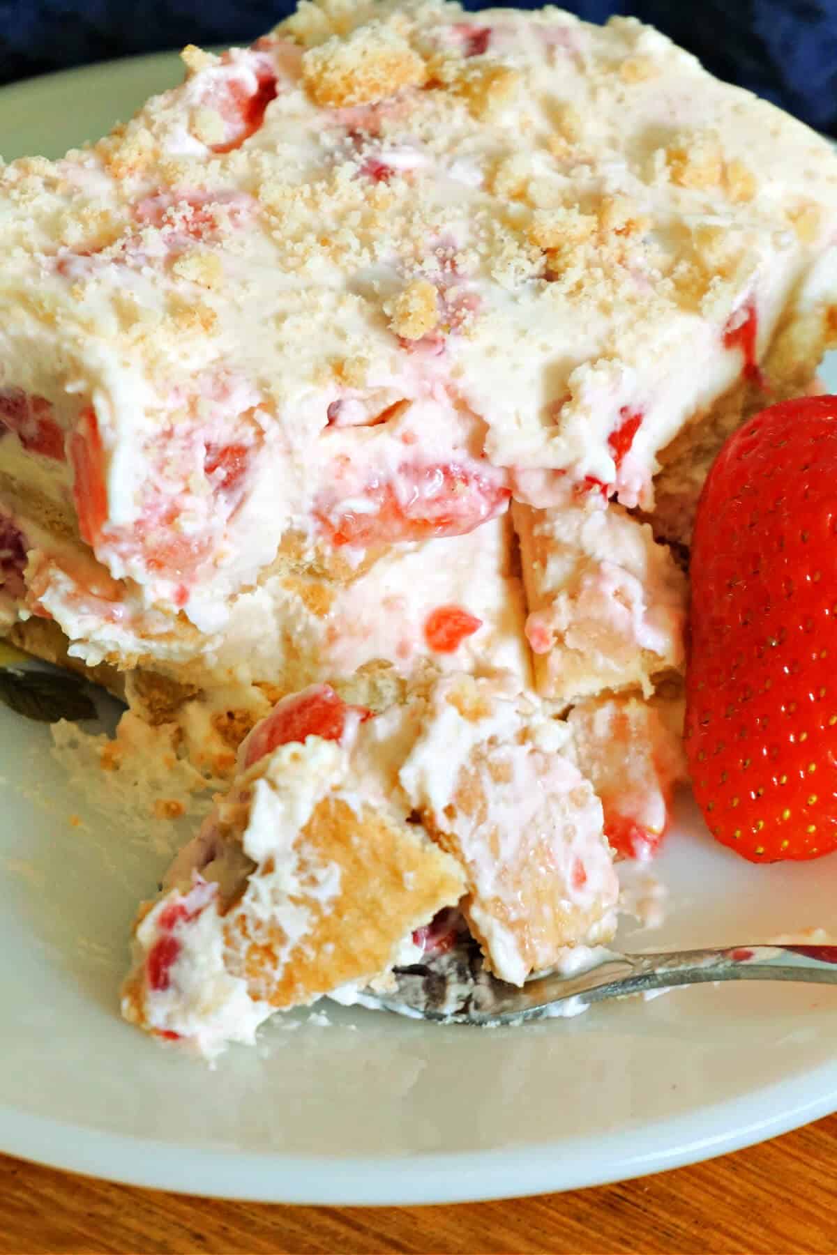 A slice of strawberry cream cake with a fresh strawberry next to it.