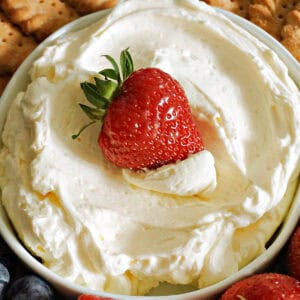 A white bowl with cheesecake dip and a strawberry dipped into it.