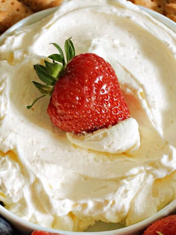 A white bowl with cheesecake dip and a strawberry dipped into it.
