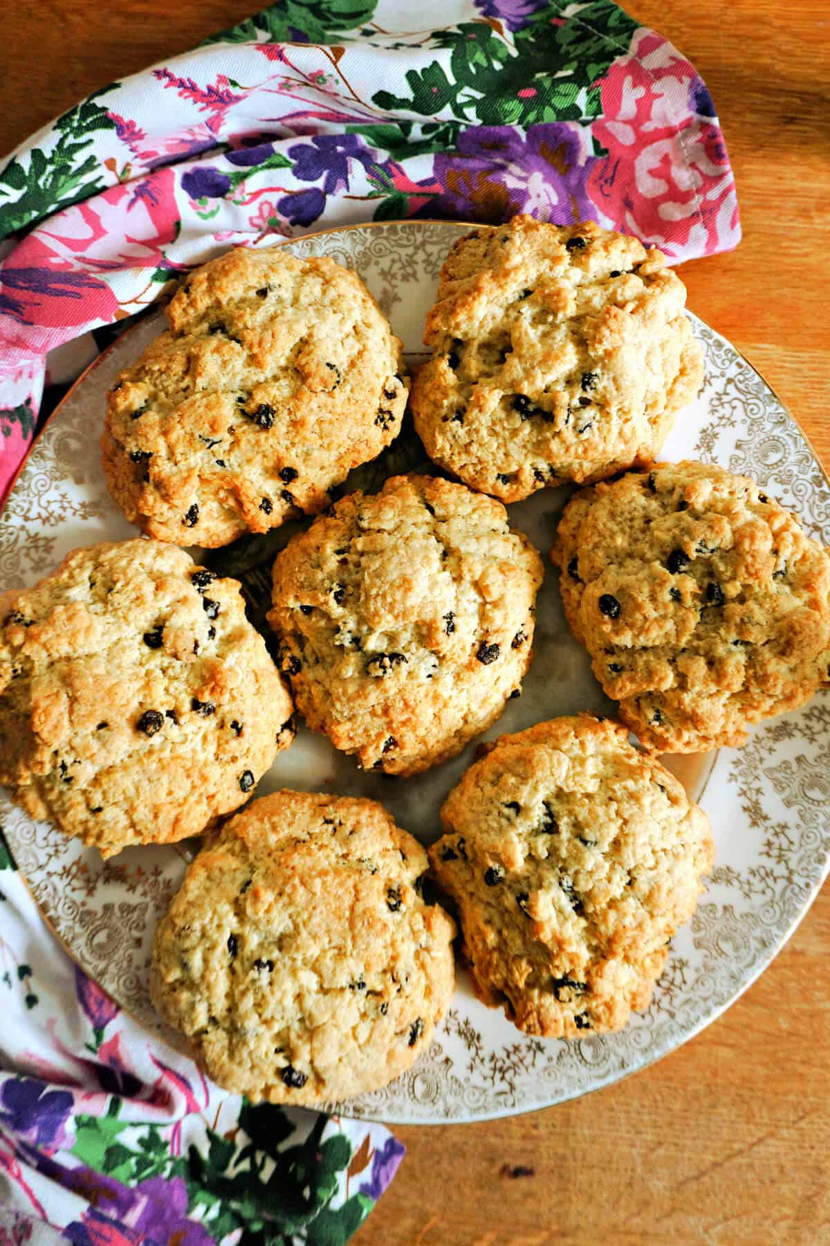 A plate with 7 rock cakes and a flowery tea towel around the plate.