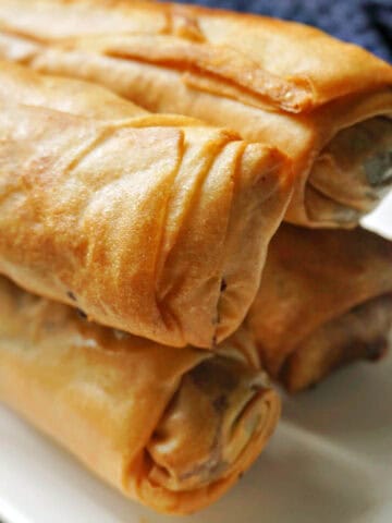 A pile of 4 spring rolls on a white plate.