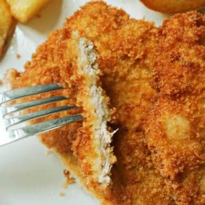 A fork piercing a sliced pork escalope which sits on top of another escalope.