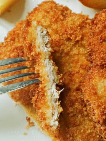 A fork piercing a sliced pork escalope which sits on top of another escalope.
