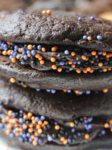 A white plate with a stack of 2 chocolate whoopie pies with Halloween sprinkles.