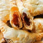 2 halves of plum turnovers on top of other whole turnovers that are drizzled with icing.