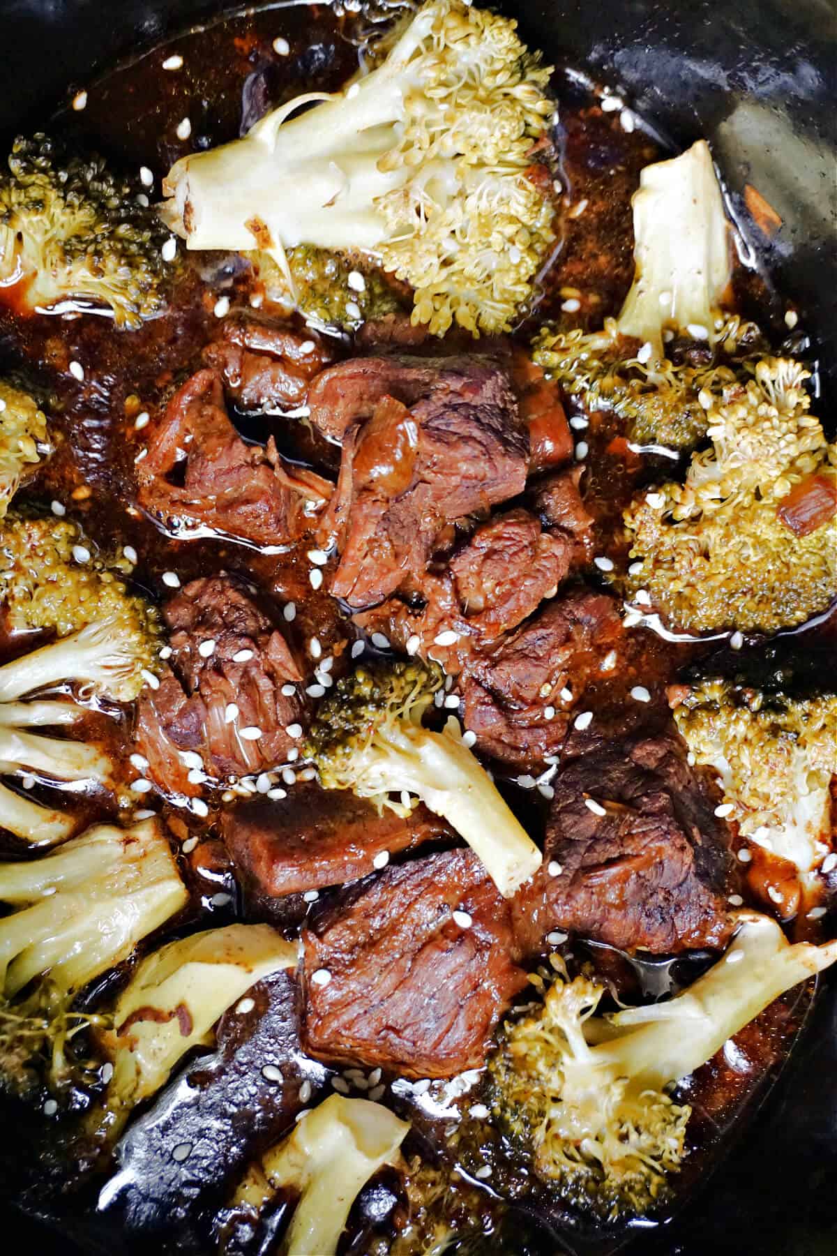 Close-up of cooked beef and broccoli florets garnished with sesame seeds.