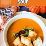 A white bowl with butternut squash soup topped with croutons, chopped parsley and chili oil.