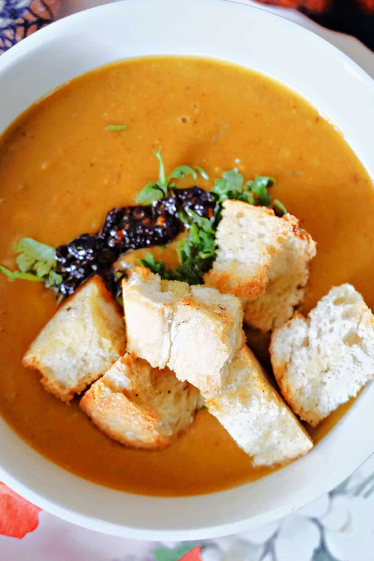 A white bowl with butternut squash soup garnished with croutons, parsley and chili oil.
