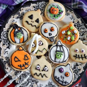 A plate with Halloween cookies and a skeleton hand grabbing the side of the plate. A purple tea towel around the plate.