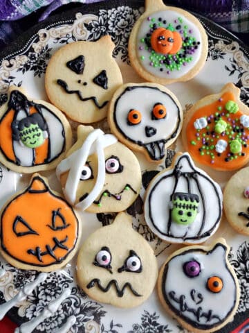 A plate with Halloween cookies and a skeleton hand grabbing the side of the plate. A purple tea towel around the plate.