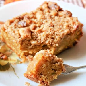 A white plate with a slice of crumble cake. A forkful of cake next to the slice.