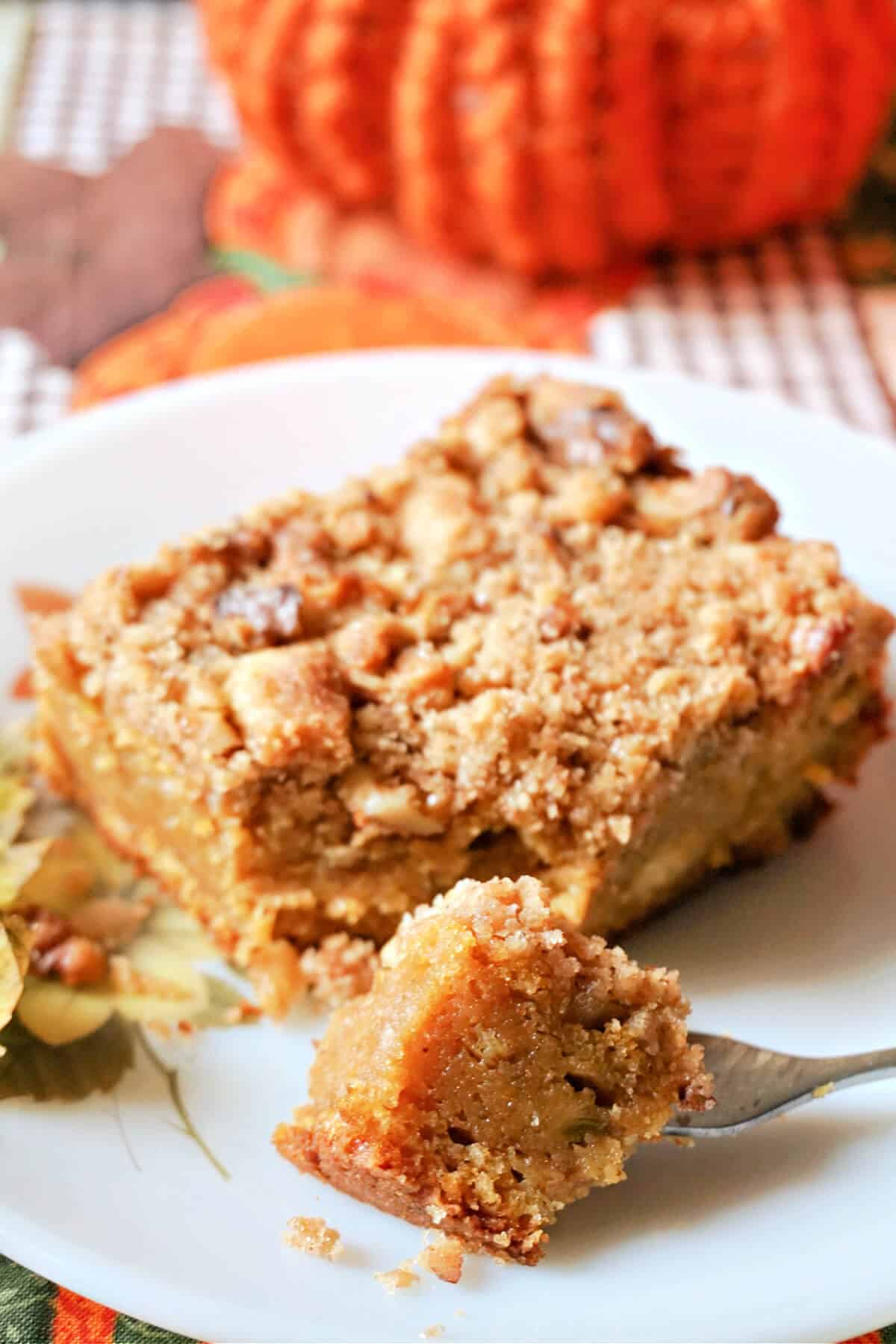 A white plate with a spice of pumpkin cake. A forkful of cake sits next to the slice of cake.
