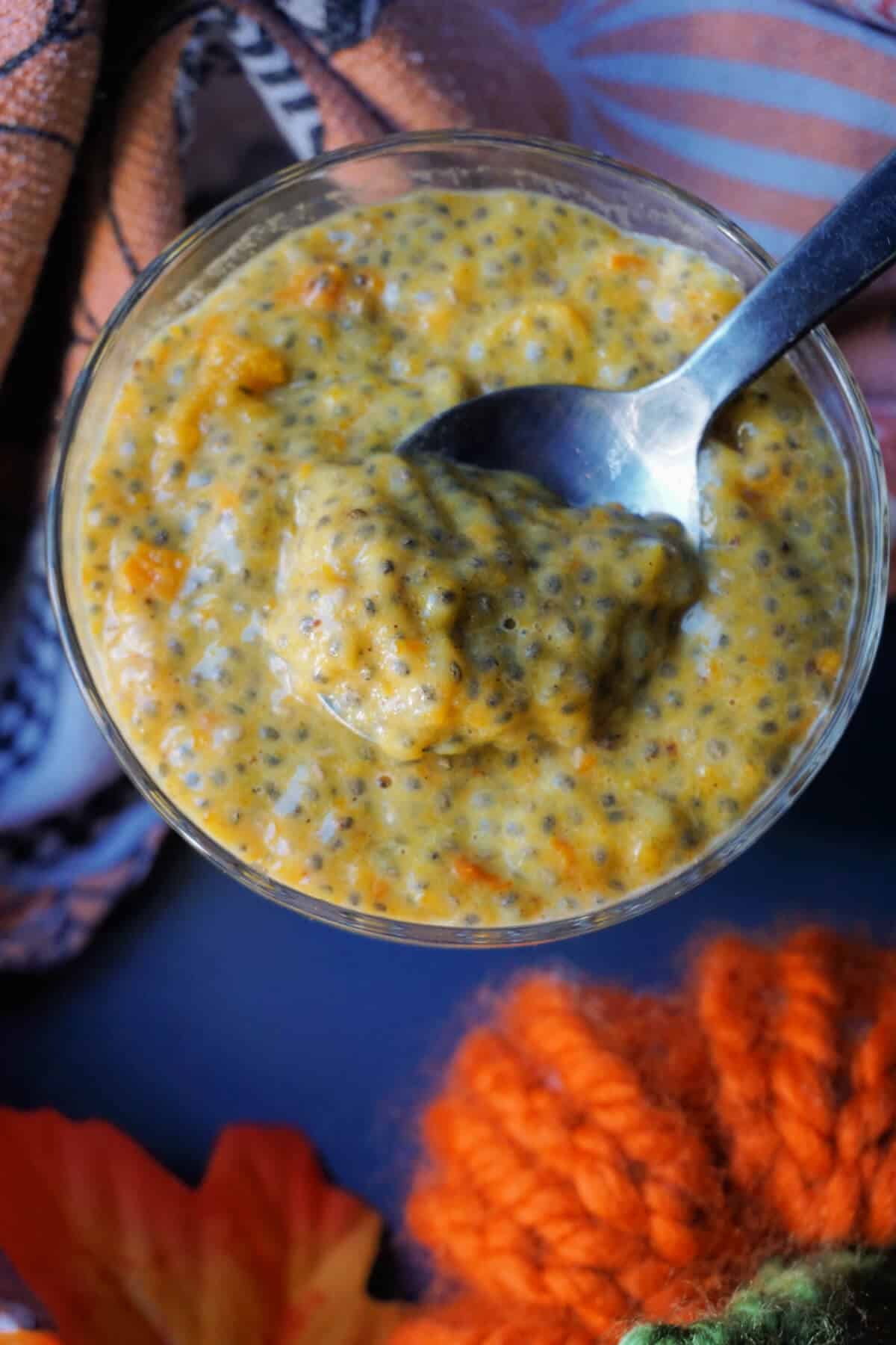 A glass with chia seed pudding made with pumpkin. A spoonful of pudding sits on top of the glass.