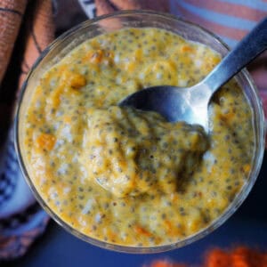 A glass with pumpkin chia seed pudding. A spoonful of pudding sits on top of the pudding.