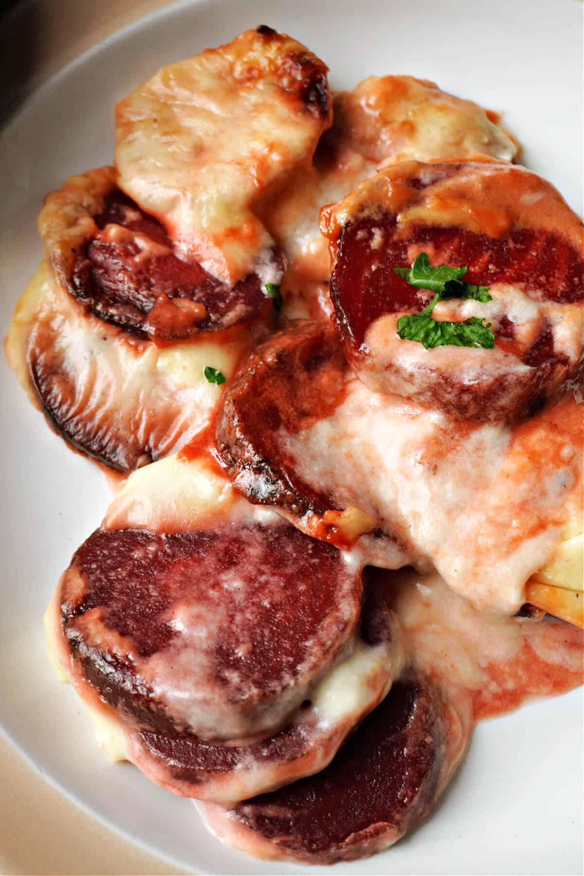 A white plate with a portion of cooked cheesy beetroot slices garnished with chopped parsley.