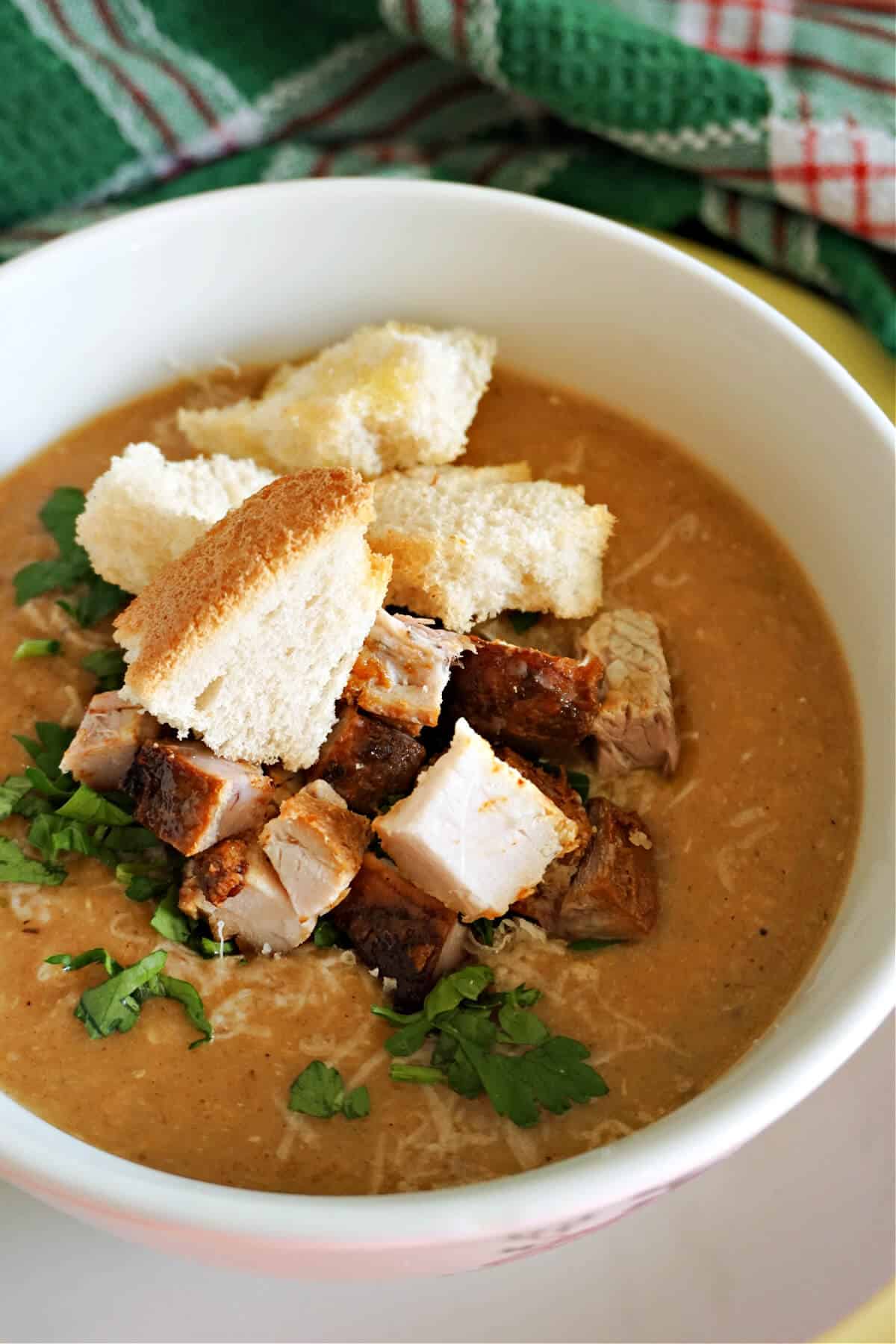 A white bowl with creamed soup topped with chopped parsley and croutons.