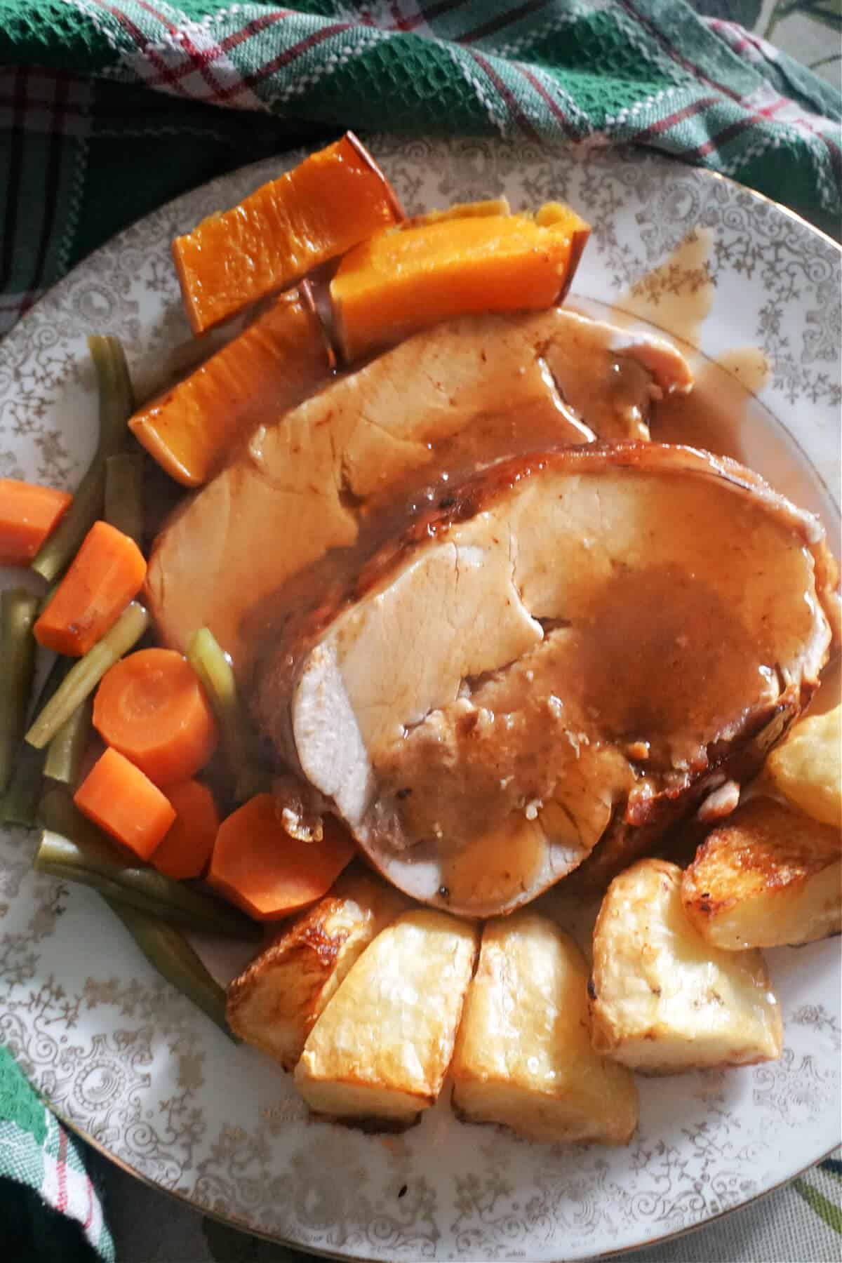 A plate with 2 slices of stuffed turkey breast and roasted vegetables smothered in gravy.
